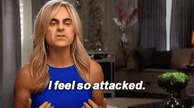 A Woman In A Blue Tank Top Is Standing In A Living Room And Saying `` I Feel So Attacked . '' GIF