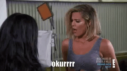 A Woman In A Blue Tank Top Is Talking To Another Woman In A Room With A Camera . GIF