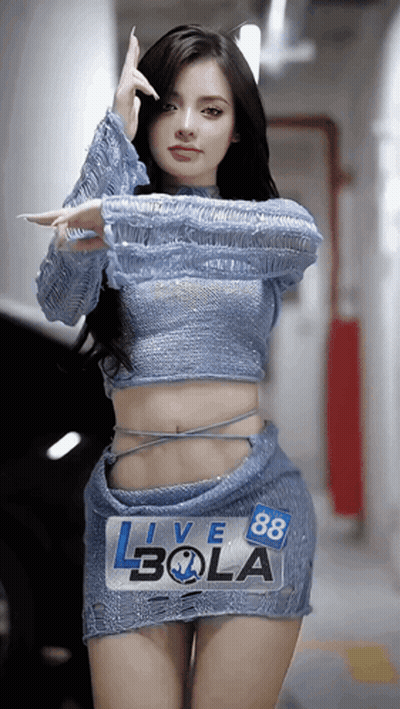 A Woman In A Blue Top And Skirt Is Standing In Front Of A Sign That Says Live 88 Bola GIF