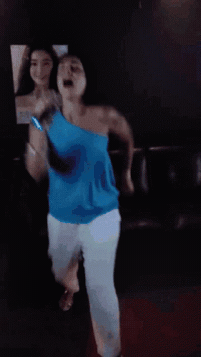 A Woman In A Blue Top Is Dancing In Front Of A Mirror GIF