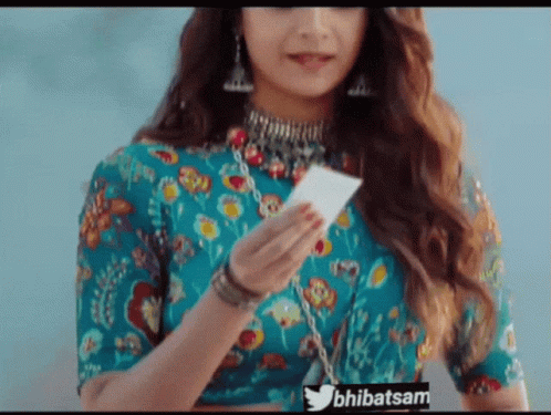 A Woman In A Blue Top Is Holding A Piece Of Paper With The Twitter Hashtag Bhibatsam Visible GIF