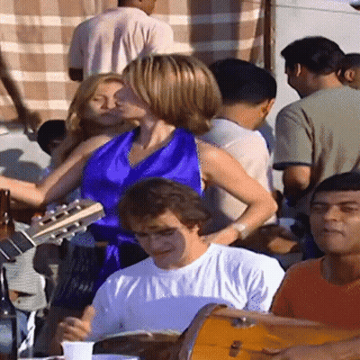 A Woman In A Blue Top Is Playing A Guitar While A Man Plays Drums GIF