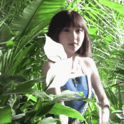 A Woman In A Blue Top Is Standing In A Jungle GIF