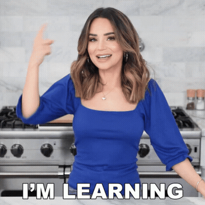 A Woman In A Blue Top Is Standing In Front Of A Stove And Says I 'M Learning GIF