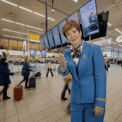 A Woman In A Blue Uniform Stands In Front Of A Sign That Says Departures Week GIF