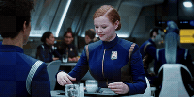 A Woman In A Blue Uniform With A Badge That Says ' Star Trek ' On It GIF