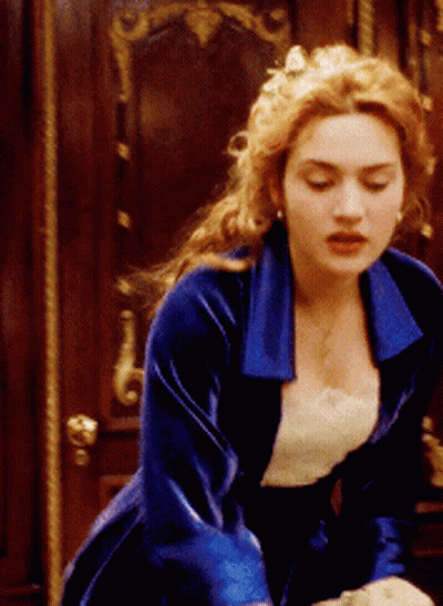 A Woman In A Blue Velvet Dress Is Standing In Front Of A Door GIF