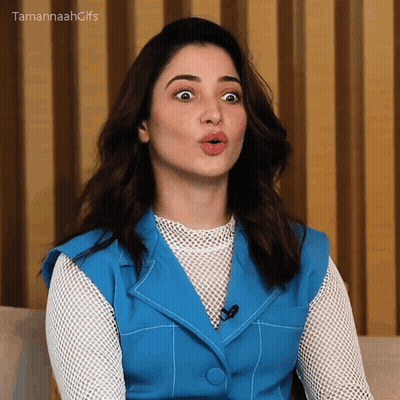 A Woman In A Blue Vest And White Shirt Is Making A Funny Face . GIF