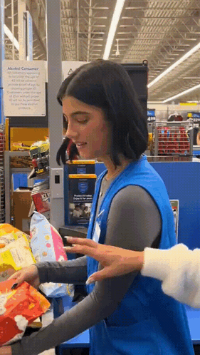 A Woman In A Blue Vest Holds A Bag Of Chips In A Store GIF