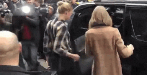 A Woman In A Brown Coat Is Getting Out Of A Car In Front Of A Crowd Of People . GIF