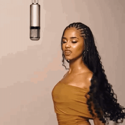 A Woman In A Brown Dress Is Standing In Front Of A Microphone . GIF