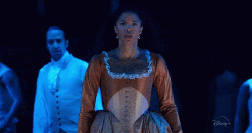 A Woman In A Brown Dress Is Standing On A Stage In Front Of A Man In A Blue Suit . GIF