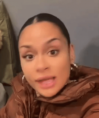 A Woman In A Brown Jacket And Earrings Is Making A Funny Face . GIF