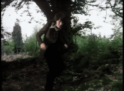 A Woman In A Brown Jacket Is Standing Under A Tree GIF