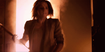 A Woman In A Brown Jacket Is Walking Down Stairs In A Dark Room GIF