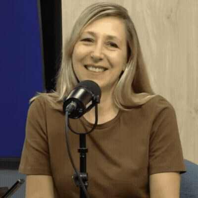 A Woman In A Brown Shirt Is Smiling In Front Of A Black Microphone GIF