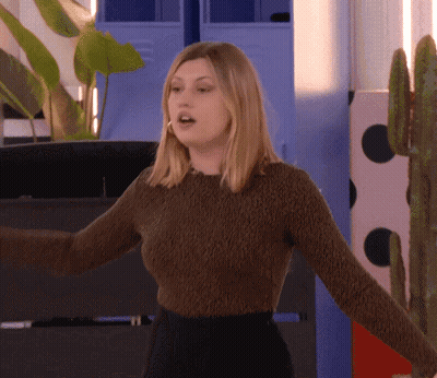 A Woman In A Brown Sweater Is Standing In Front Of A Cactus GIF