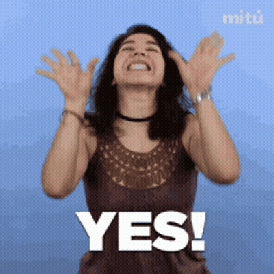 A Woman In A Brown Tank Top Says Yes With Her Hands In The Air GIF