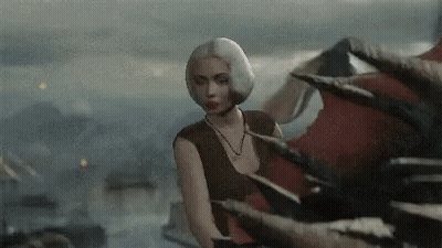 A Woman In A Brown Top Stands In Front Of A Dragon 'S Tail GIF
