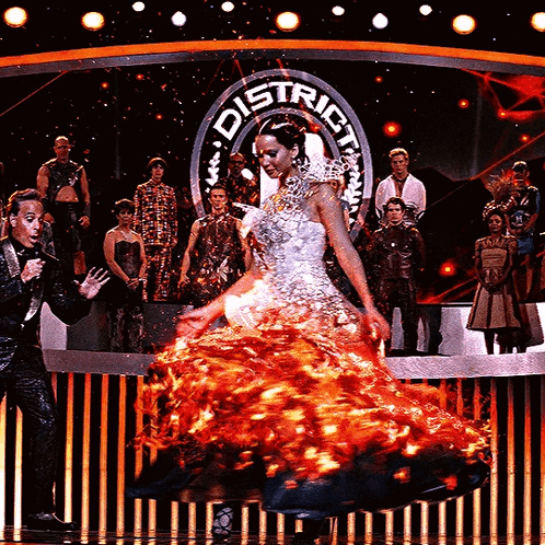 A Woman In A Burning Dress Is Dancing On A Stage In Front Of A Sign That Says District GIF