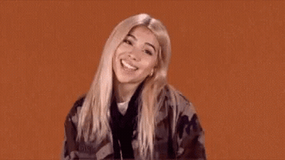A Woman In A Camouflage Jacket Is Making A Funny Face And Giving A Thumbs Up . GIF