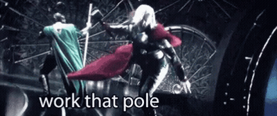 A Woman In A Cape Is Standing On A Pole With The Words `` Work That Pole '' Above Her . GIF