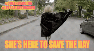 A Woman In A Cape Is Walking Down A Street With The Words She 'S Here To Save The Day GIF