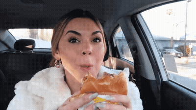 A Woman In A Car Is Eating A Sandwich With Her Mouth Open GIF