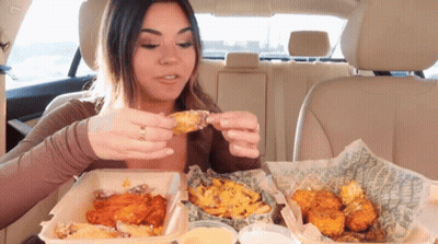 A Woman In A Car Is Eating Chicken Wings GIF