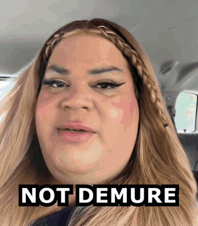A Woman In A Car With The Words Not Demure Above Her Head GIF
