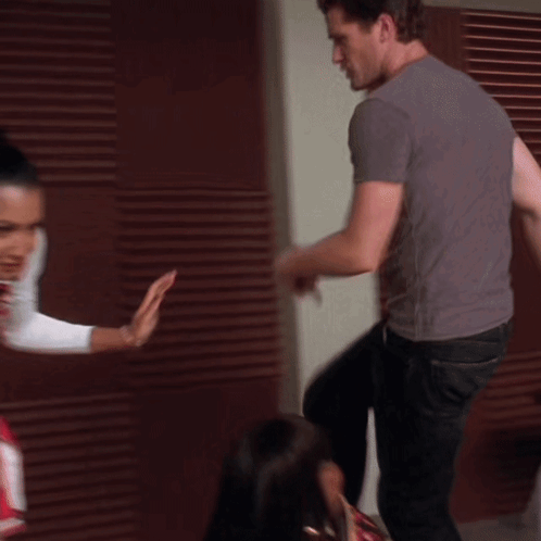 A Woman In A Cheerleader Outfit Is Standing Next To A Man In A Grey Shirt GIF