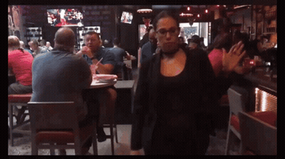 A Woman In A Choker Is Walking In A Crowded Restaurant GIF