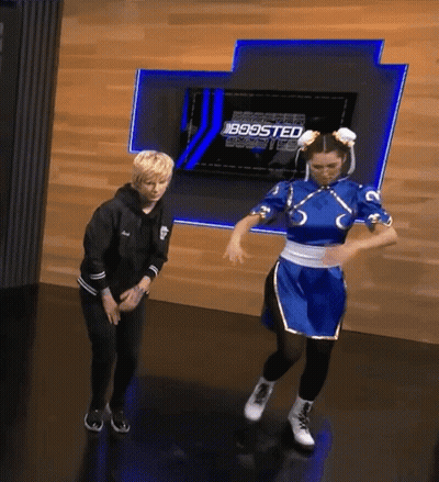 A Woman In A Chun Li Costume Is Dancing In Front Of A Wall That Says Boosted GIF
