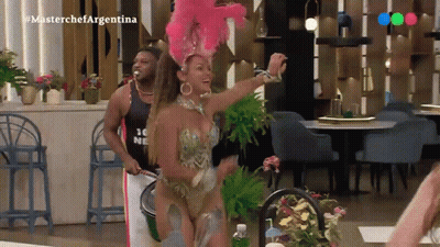 A Woman In A Colorful Costume Is Dancing In Front Of A Man Wearing A Shirt That Says Masterchef Argentina .. GIF