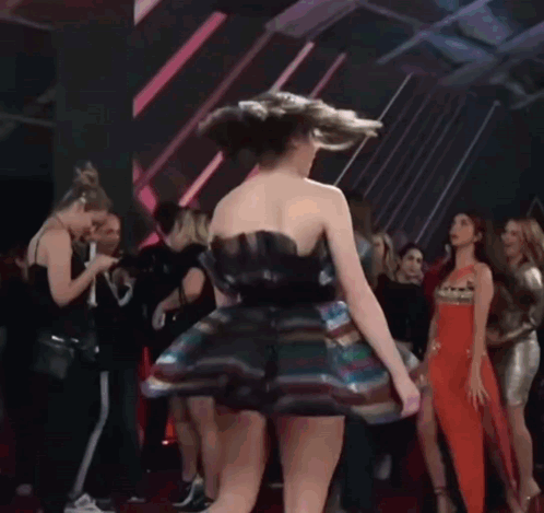 A Woman In A Colorful Dress Is Dancing In Front Of A Crowd Of People GIF