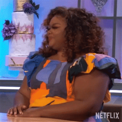 A Woman In A Colorful Dress Is Sitting At A Table With Her Hands On Her Hips . GIF
