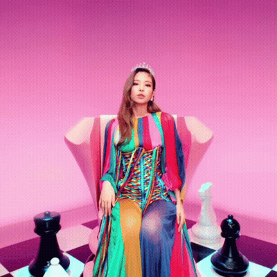 A Woman In A Colorful Dress Is Sitting On A Chair With Chess Pieces Around Her GIF