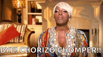A Woman In A Colorful Dress Is Standing In A Living Room And Says `` Bye ! Chorizo Chomper ! '' GIF