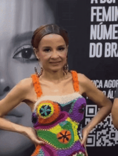 A Woman In A Colorful Dress Stands In Front Of A Sign That Says Feminin Nume Do Br GIF