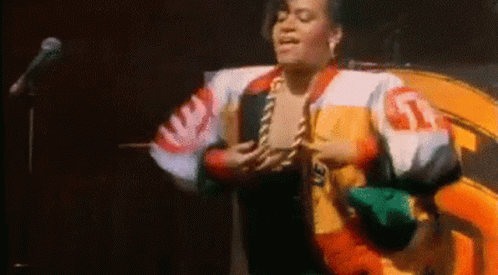 A Woman In A Colorful Jacket Is Standing In Front Of A Microphone . GIF