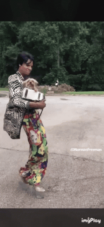 A Woman In A Colorful Outfit Is Holding A Dog In Her Arms .. GIF
