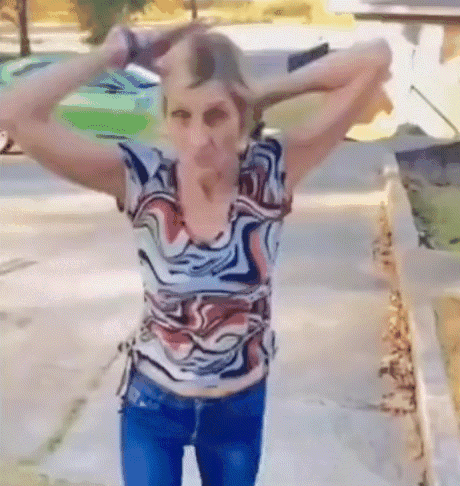 A Woman In A Colorful Shirt Is Standing On A Sidewalk With Her Arms Outstretched GIF