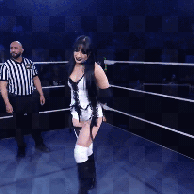 A Woman In A Corset Is Walking In A Ring With A Referee GIF