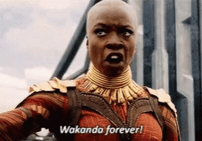 A Woman In A Costume Is Standing In Front Of A Building And Says Wakanda Forever . GIF