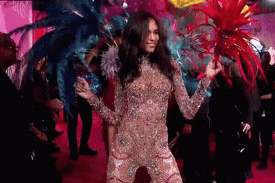 A Woman In A Costume With Feathers On Her Head Is Dancing On A Pink Carpet . GIF