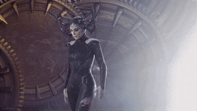 A Woman In A Costume With Horns Is Standing In Front Of A Clock That Says ' X ' On It GIF
