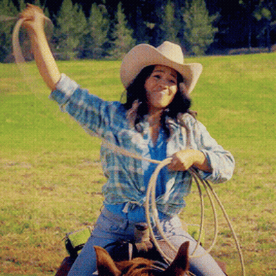 A Woman In A Cowboy Hat Is Holding A Lasso While Riding A Horse GIF