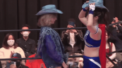 A Woman In A Cowboy Hat Is Standing Next To Another Woman In A Blue Outfit . GIF