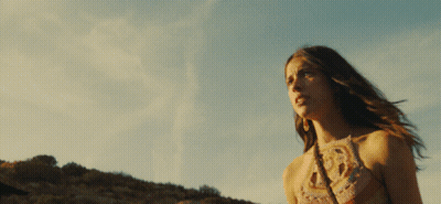 A Woman In A Crocheted Top Stands In Front Of A Cloudy Sky GIF
