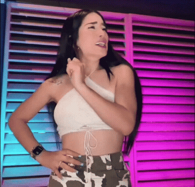 A Woman In A Crop Top And Camo Shorts Is Standing In Front Of A Purple Wall . GIF